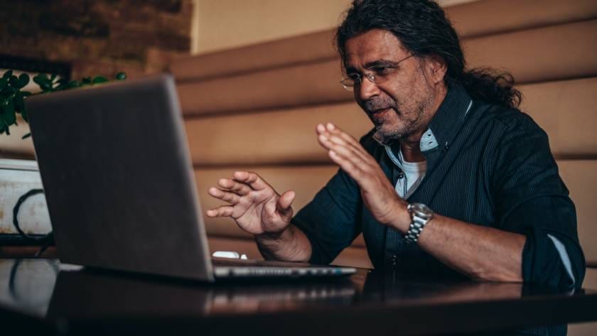Senior hispanic cuban man using his laptop for an online video call in a cafe