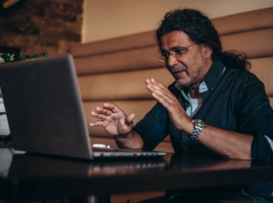 Senior hispanic cuban man using his laptop for an online video call in a cafe