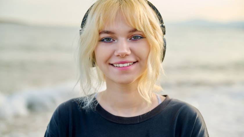 Portrait of smiling teenage female wearing headphones, on beach, close-up face, smile with teeth